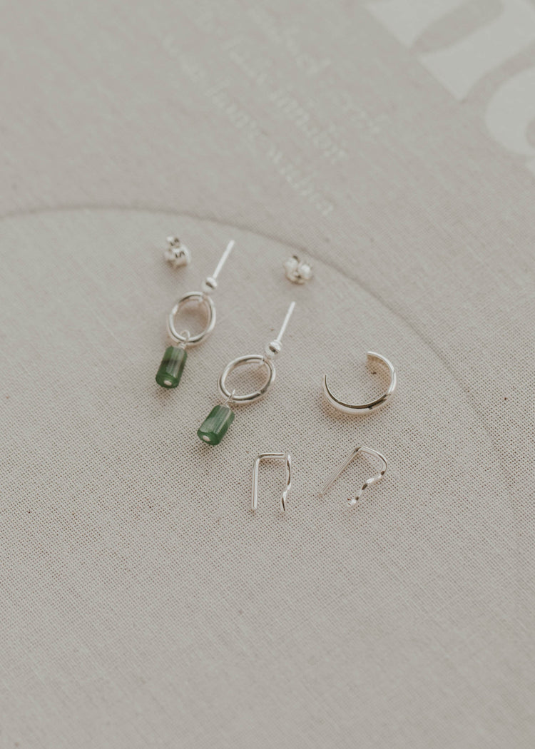 Collection of small silver and green earrings on a light gray background