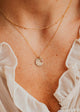Close-up of a person wearing a Hello Adorn gold necklace with a pendant, with a white blouse in the background.