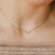 A close-up image of a woman wearing a gold chain necklace with a simple, uterus shaped pendant.
