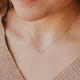 Close-up of a person wearing a delicate gold necklace with a uterus design.