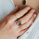 Close-up of a person wearing gold necklaces and rings with green stones.