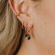 Close-up of an ear wearing gold hoop earrings with a black gemstone.