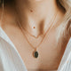 Close-up of a person wearing a necklace with a pendant, dressed in a white shirt.