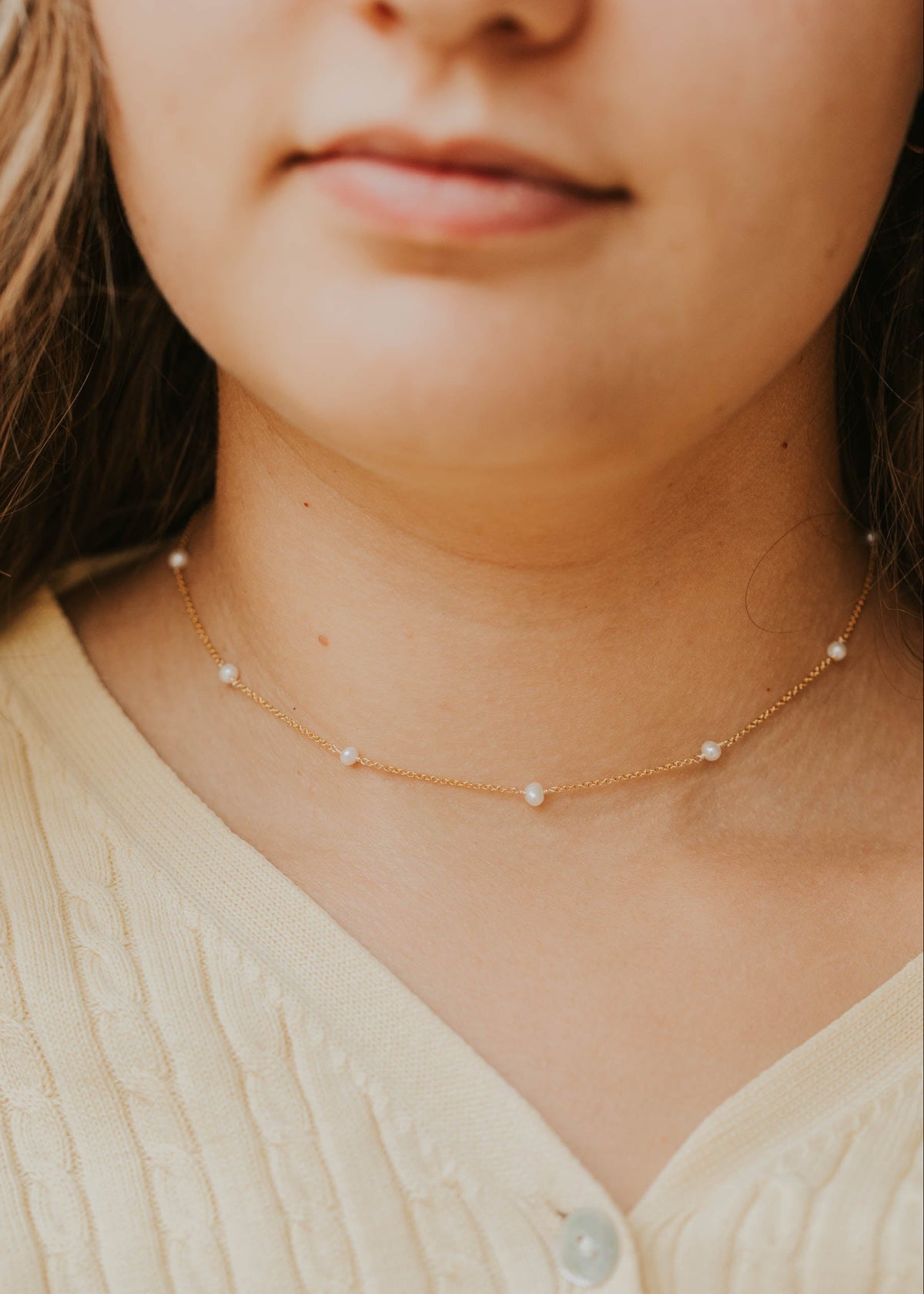 Close-up of a person wearing a delicate pearl necklace with a blurred background