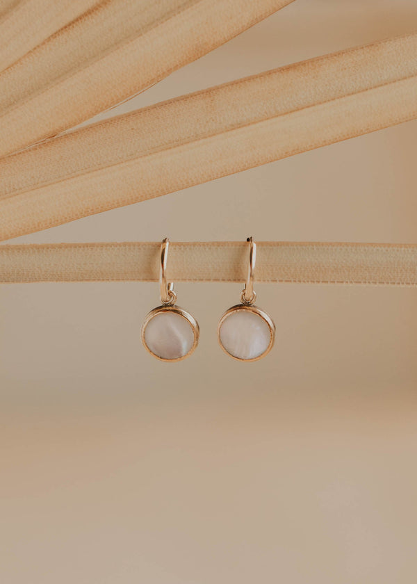 Gold earrings with round stones on a beige background