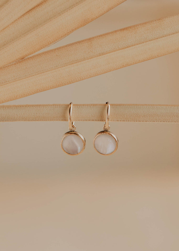 Gold earrings with round stones on a beige background