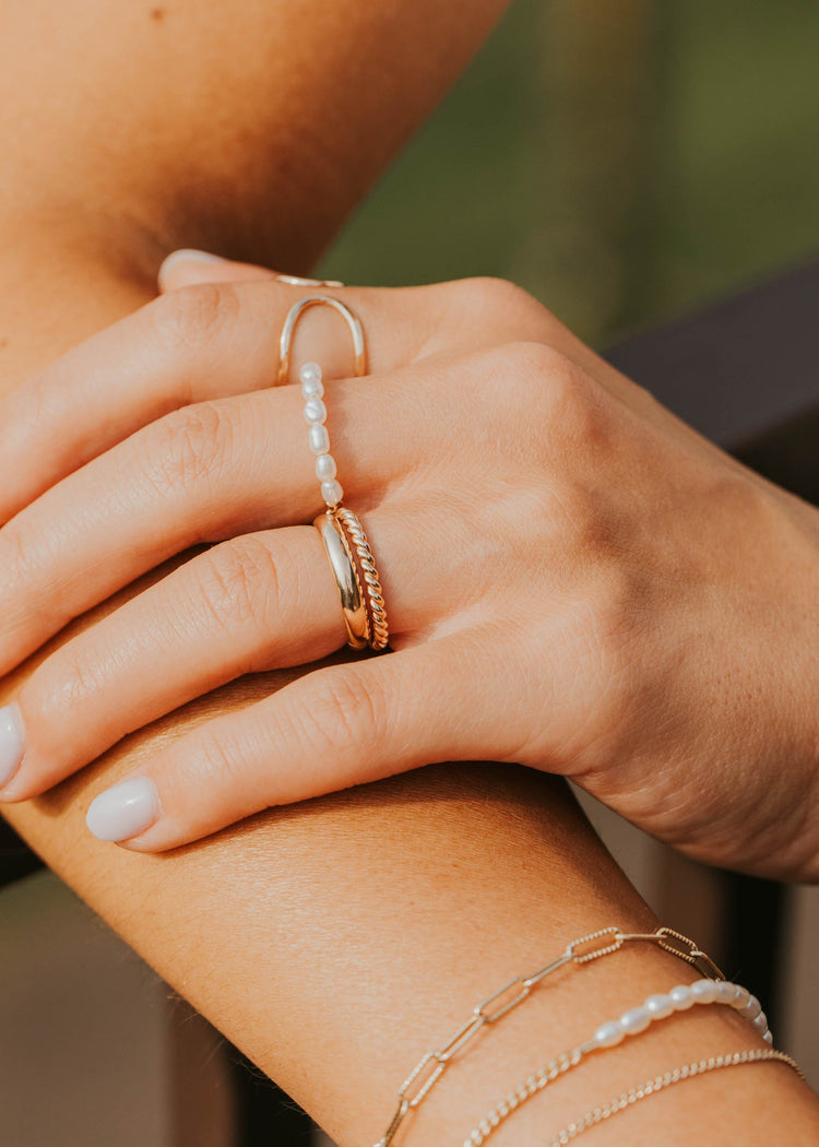Close-up of a hand wearing multiple gold rings and bracelets against a blurred background