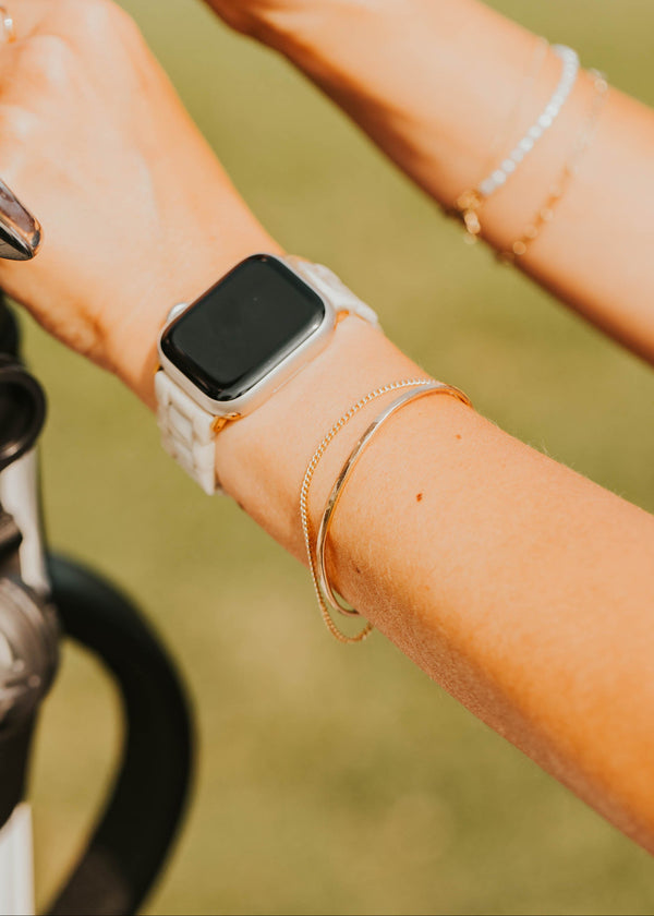 Person wearing a smartwatch with multiple bracelets on a blurred background