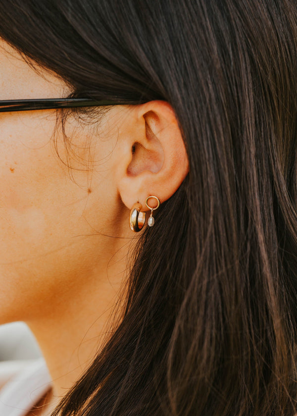 Close-up of an ear wearing gold hoop earrings with dark hair.