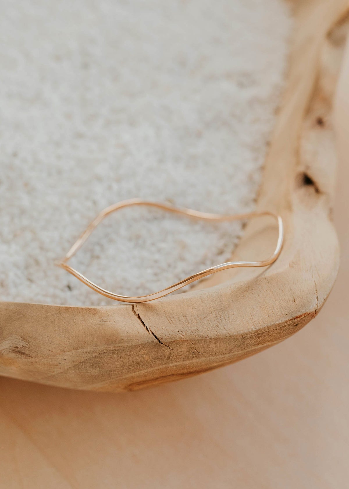 Gold bangle bracelet on a textured surface with a wooden bowl