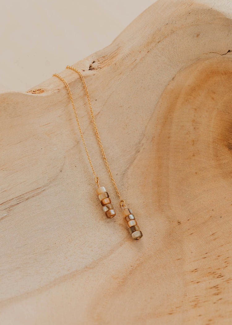 Gold earrings with beaded pendant on a wooden surface