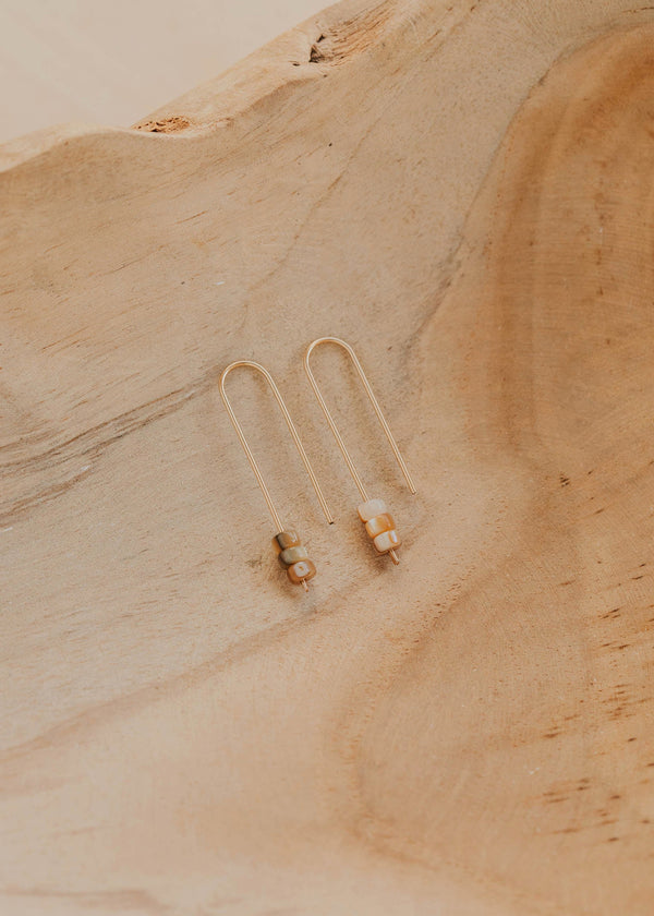 Gold earrings on a textured beige surface