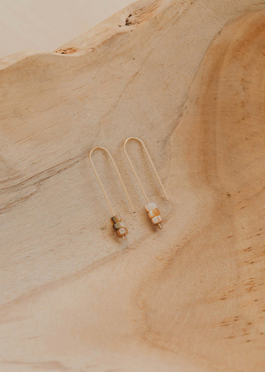 Gold earrings on a textured beige surface