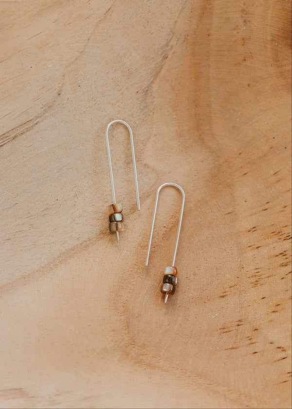 Pair of U-shaped threader earrings on a sandy surface