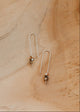 Pair of U-shaped threader earrings on a sandy surface