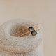 Pair of gold and black earrings on a textured stone surface with a soft beige background