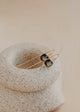 Pair of gold and black earrings on a textured stone surface with a soft beige background