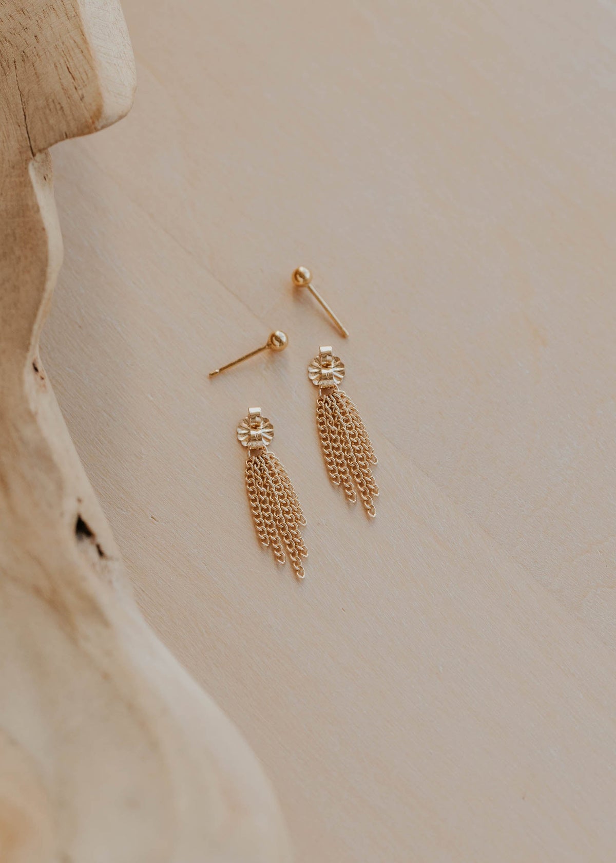 Gold feather-shaped earrings on a neutral background