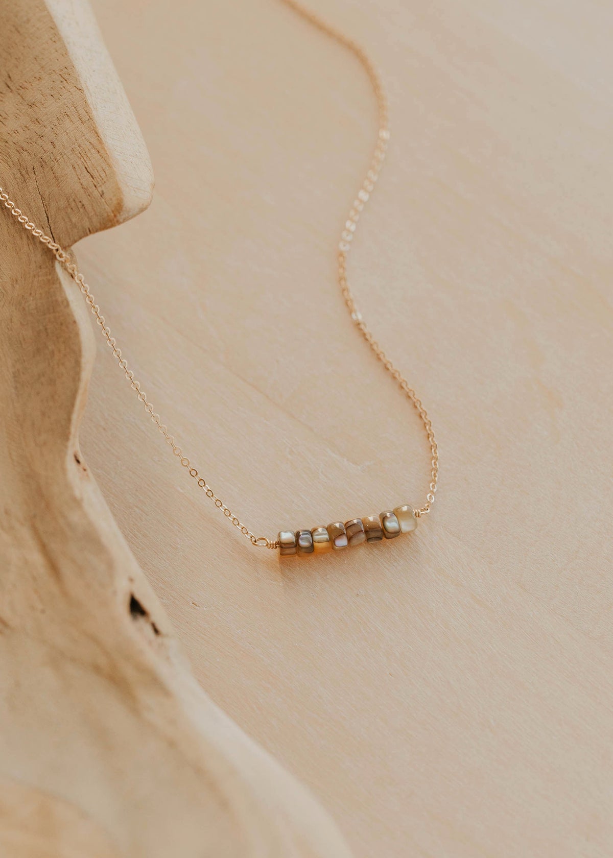 Delicate gold necklace with small beads on a beige stone surface