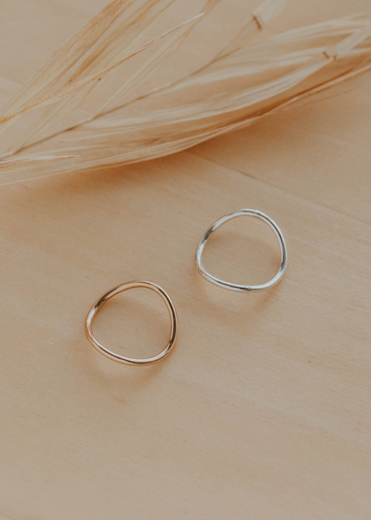 Two gold rings on a beige surface with dried grass.