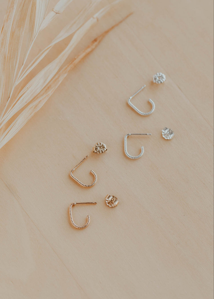 Set of gold and silver earrings on a beige surface with a leaf