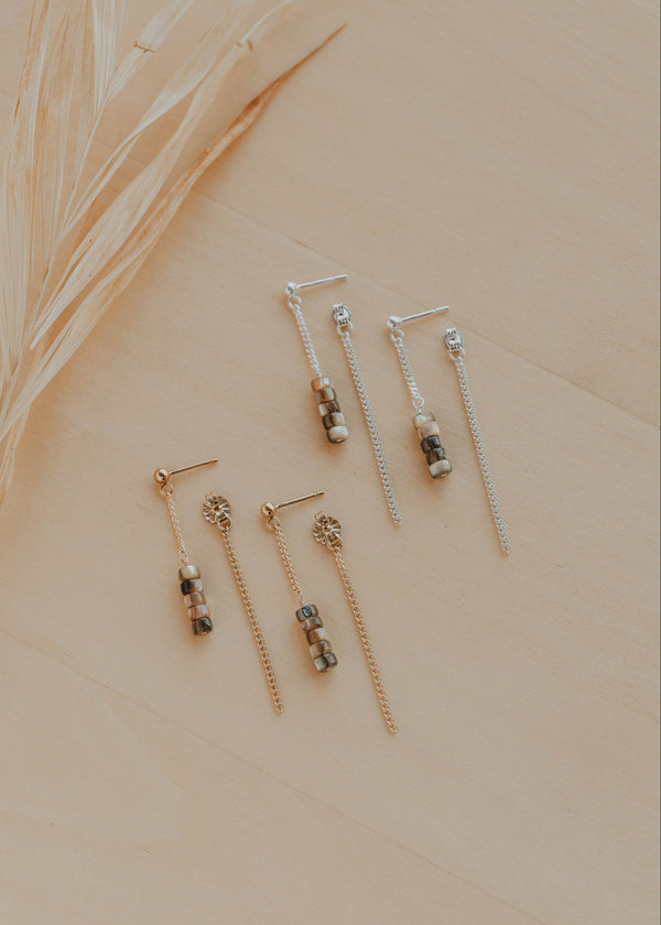 Set of gold earrings on a beige surface with dried grass