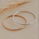 Two gold hoop bracelets on a beige surface with a blurred background