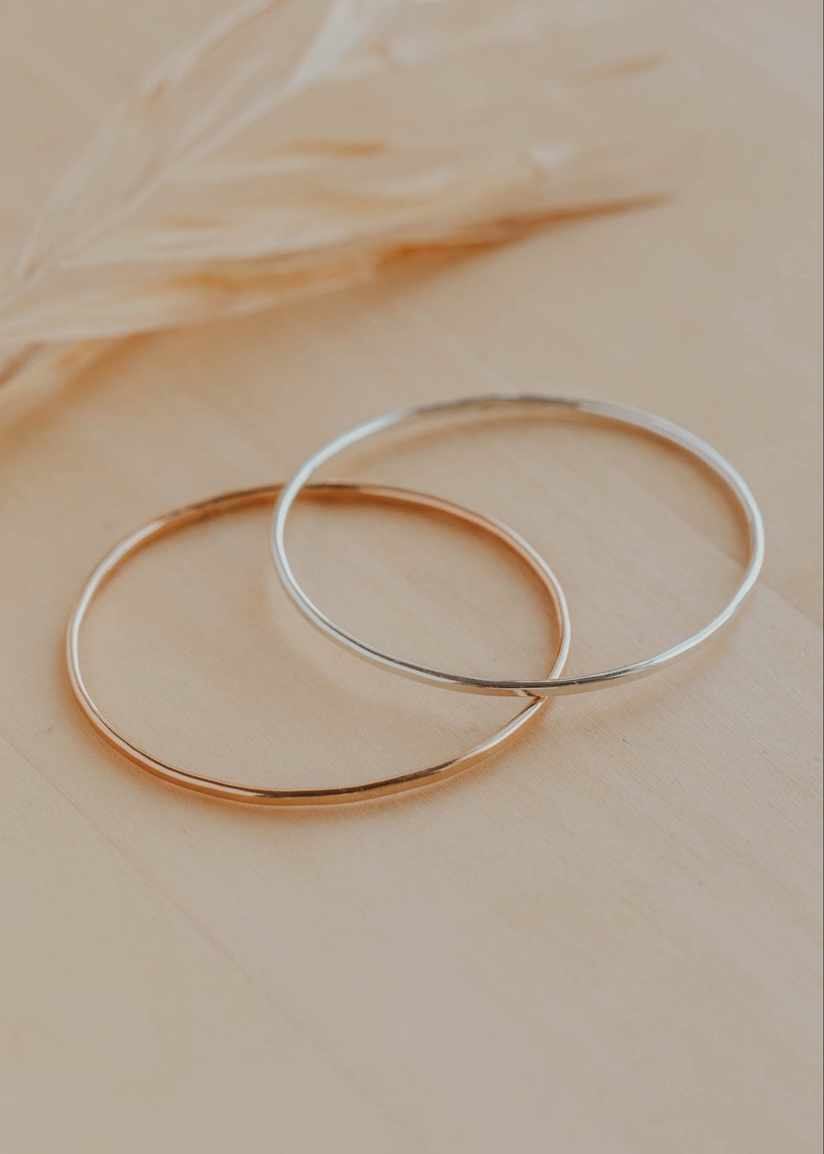 Two gold hoop bracelets on a beige surface with a blurred background