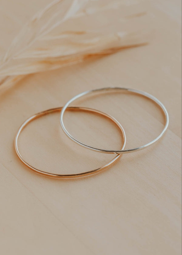 Two gold hoop bracelets on a beige surface with a blurred background