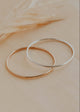 Two gold hoop bracelets on a beige surface with a blurred background