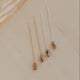 Three delicate earrings on a beige surface with a blurred leaf in the background