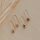 Pair of gold earrings with small beads on a beige surface with dried grass.