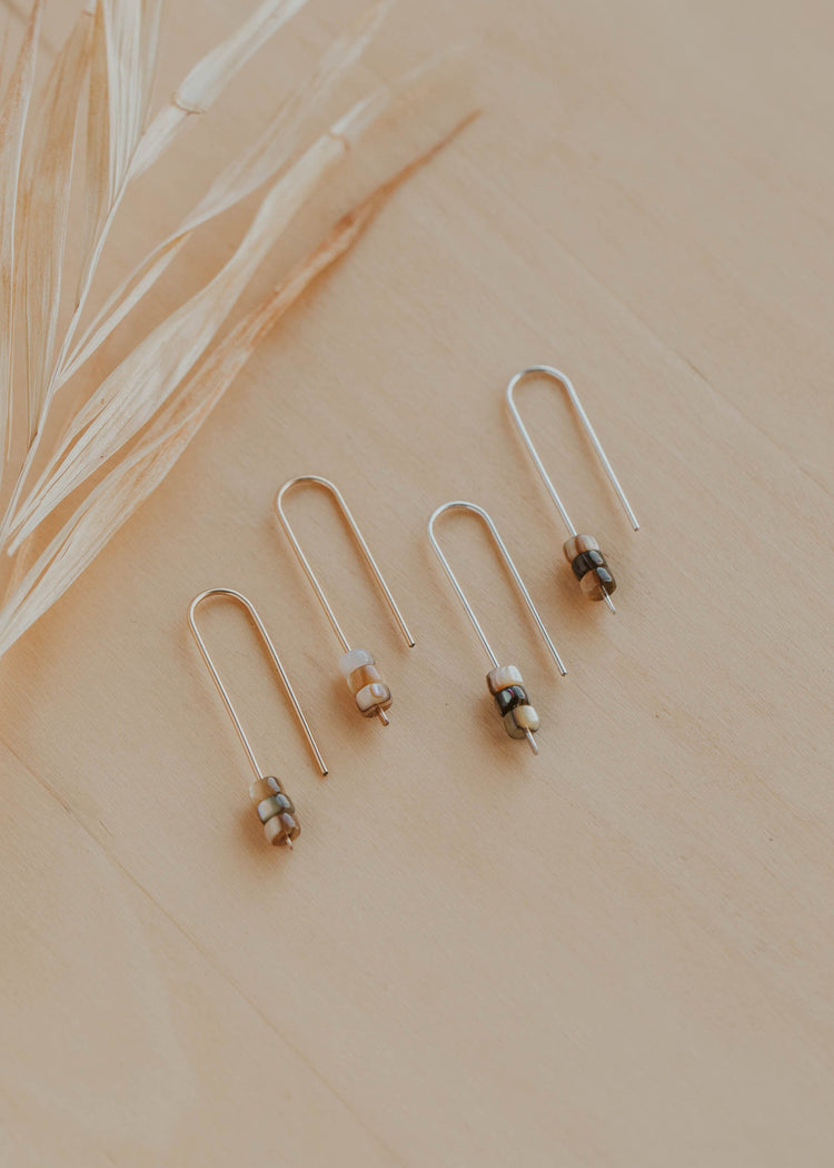 Pair of gold earrings with small beads on a beige surface with dried grass.