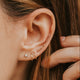 Close-up of an ear with gold earrings and hair being adjusted.