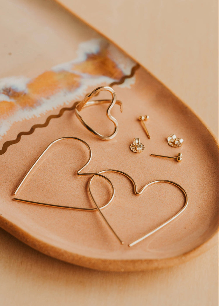 Gold heart-shaped earrings on a beige ceramic dish