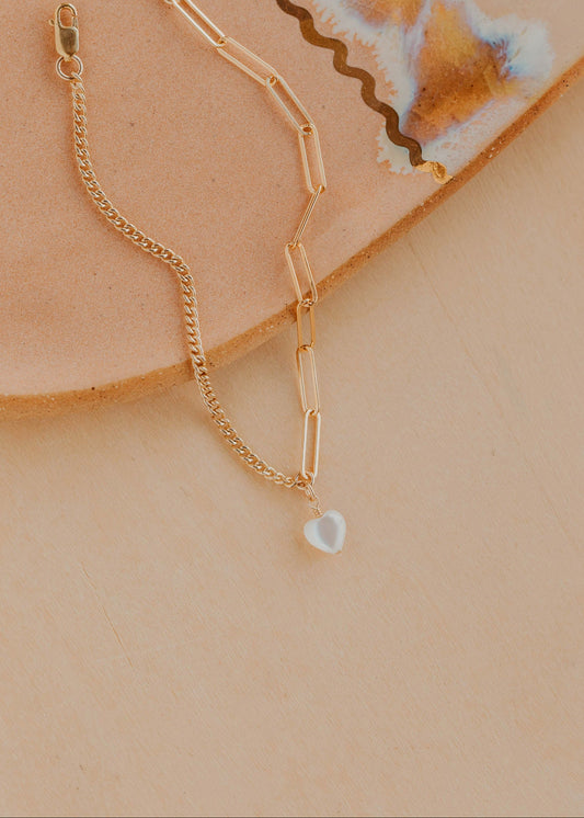 Gold chain bracelet with a heart pendant on a beige surface