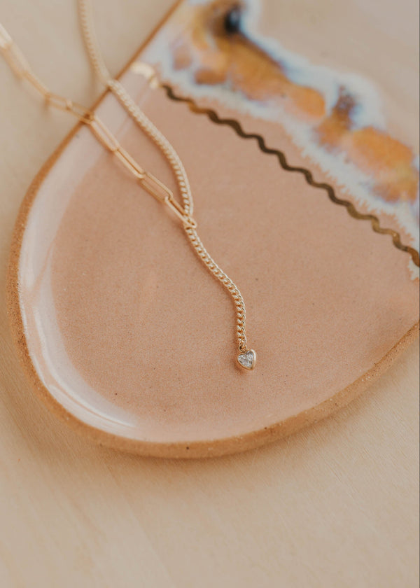 Gold necklace with a small diamond pendant on a beige plate