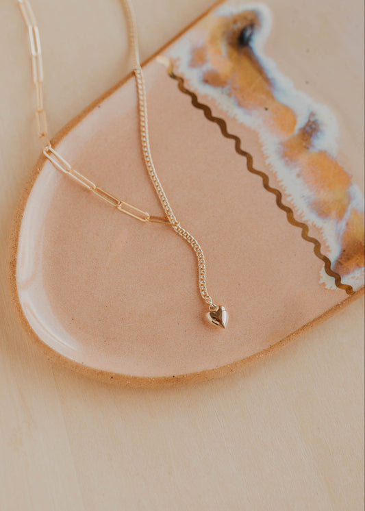 Gold necklace with a heart pendant on a beige dish