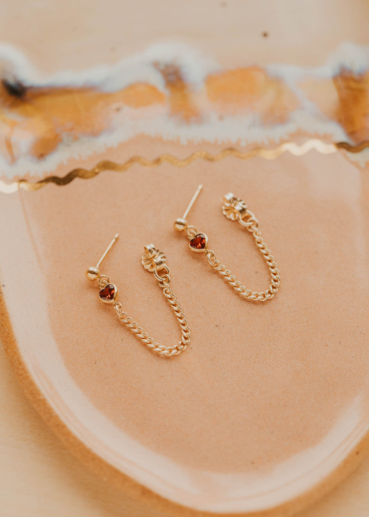 Gold earrings with red gemstones on a beige surface