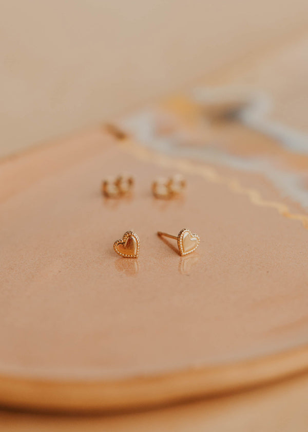 Gold heart-shaped earrings on a beige surface
