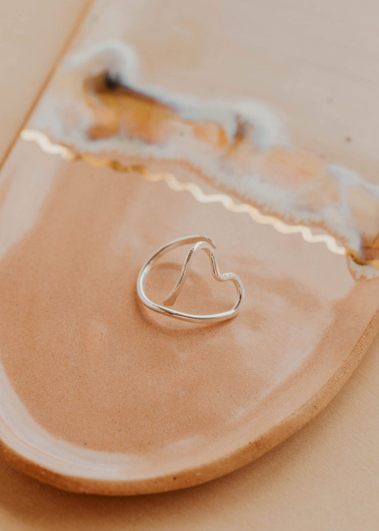 Heart-shaped silver ring on a beige ceramic dish