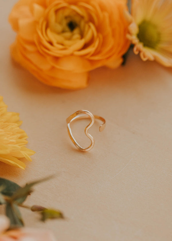 Heart-shaped gold ring on a light surface with yellow flowers