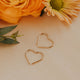 Gold heart-shaped earrings on a light surface with orange flowers and green leaves.