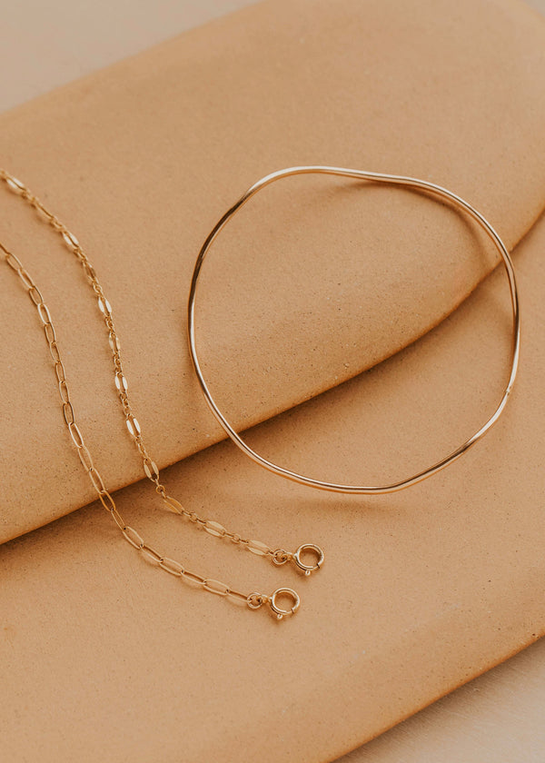 Gold bracelet and chain on a beige surface