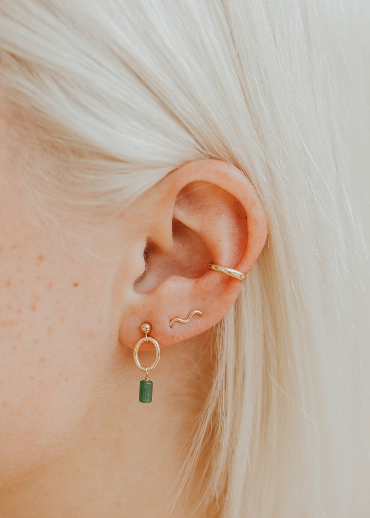 Close-up of an ear wearing gold hoop earrings with a green gemstone.