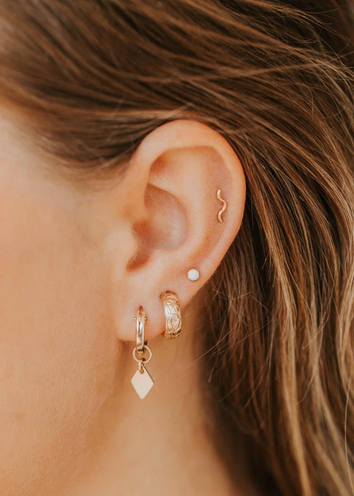 Close-up of an ear with gold earrings and an opal, with blurred hair in the background