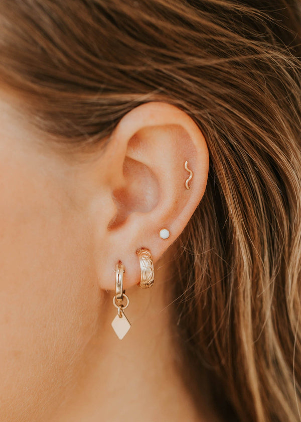 Close-up of an ear with gold earrings and an opal, with blurred hair in the background