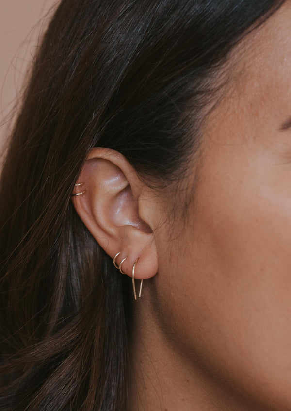 Tiny horseshoe gold threader earrings by Hello Adorn styled in an ear with double up cuff and twist earrings.