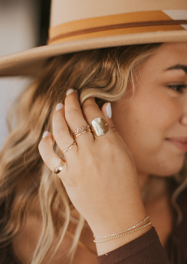 A jewelry idea and an idea of how to stack rings on fingers using a squiggle ring, woven ring, thin ring, large circle ring, gold ring band, a wave ring, and a thick ring paired with two chain bracelets showing gold and silver jewelry together by Hello Adorn.