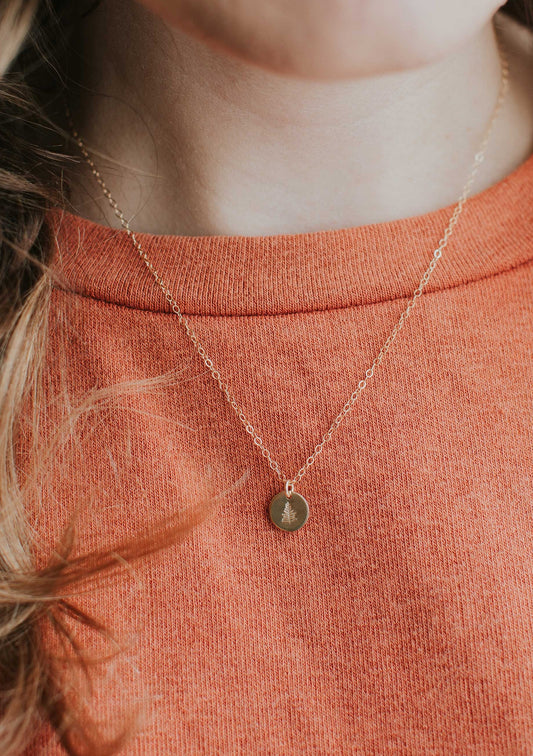 A custom necklace pendant with an evergreen tree stamped onto this gold necklace by Hello Adorn.